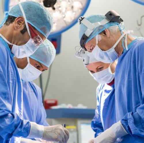 Portrait of team of multiethnic surgeons at work in a operation theatre. Several doctors surrounding patient on operation table during their work. Team surgeons at work in operating room.