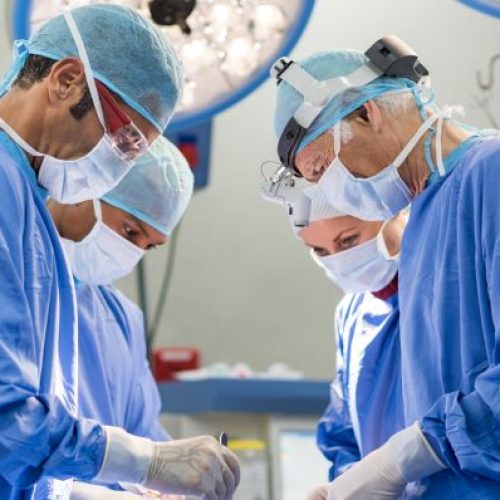 Portrait of team of multiethnic surgeons at work in a operation theatre. Several doctors surrounding patient on operation table during their work. Team surgeons at work in operating room.